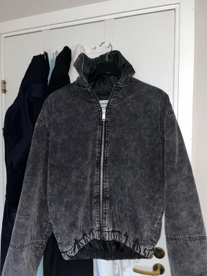Svart tvättad bomberjacka Weekday - Snygg svart bomberjacka från Weekday i tvättad look. Jackan har dragkedja framtill, hög krage och quiltat foder. Resår i midjan och vid ärmsluten ger en schysst passform. Perfekt för dig som gillar streetwear och vill ha en unik jacka.