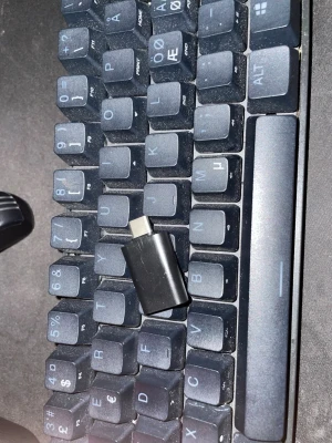 Steelseries apex pro mini - Säljer ett svart SteelSeries tangentbord med nordisk layout och en liten svart USB-C-adapter. Tangentbordet har tydliga vita tecken på knapparna och är gjort i plast. Perfekt för gaming eller skrivbordsarbete.