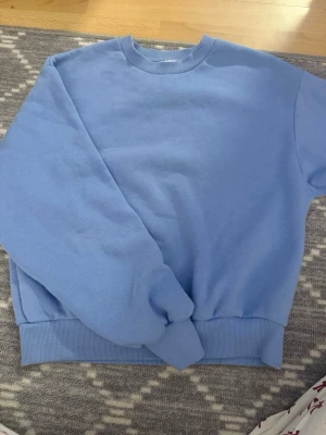 Ljusblå basic hoodie - En stilren ljusblå hoodie med rund halsringning och ribbade muddar vid ärmslut och nederkant. Hoodien har en relaxed fit och är gjord i mjukt material, perfekt för en chill och enkel look.