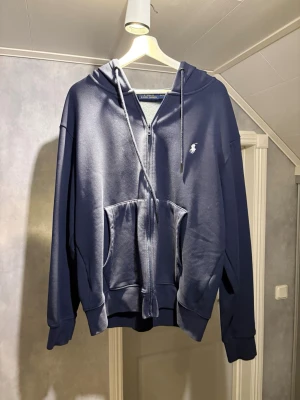 Mörkblå hoodie från Polo Ralph Lauren - Snygg mörkblå hoodie från Polo Ralph Lauren i storlek XL med dragkedja framtill och klassisk vit logga på bröstet. Hoodien har huva med dragsko och en stor känguruficka. Tillverkad i mjukt material som känns skönt mot huden. Perfekt för en avslappnad och stilren look. Använd fåtal gånger, inga fula märken eller skav. Ser som ny ut. Skickas samma dag eller dagen efter köpet, pris går att diskutera. mvh