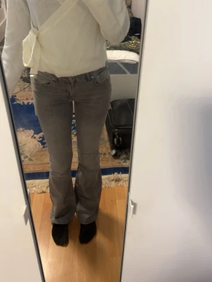 Grå bootcut jeans med hög midja - Säljer ett par gråa bootcut jeans med hög midja och klassiska fem fickor. Jeansen har en snygg tvätt och är tillverkade i ett stretchigt denimtyg som sitter bekvämt. Perfekta för dig som gillar en retroinspirerad look.