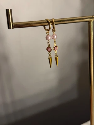 Guldörhängen med pärlor och rosa stenar - Säljer ett par unika örhängen i guldton med ljusrosa pärlor, rosa stenar och spetsiga hängen. Örhängena har en cool mix av material och färger som ger en trendig vibe. Perfekta för dig som vill sticka ut lite extra med dina accessoarer.