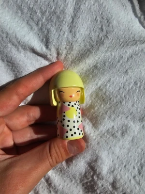Söt kokeshi-docka med prickigt mönster - En liten kokeshi-docka i trä med ljusgult hår och vit kropp dekorerad med svarta prickar och pastellfärgade detaljer. Dockan har ett gulligt ansikte med stängda ögon och röd mun. Perfekt som dekoration eller samlarobjekt.