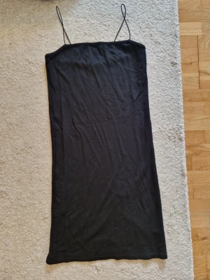Svart klänning med tunna axelband - En enkel och stilren svart klänning med tunna axelband och rak passform. Klänningen är gjord i ett mjukt material och har en minimalistisk look som passar perfekt till många olika stilar.