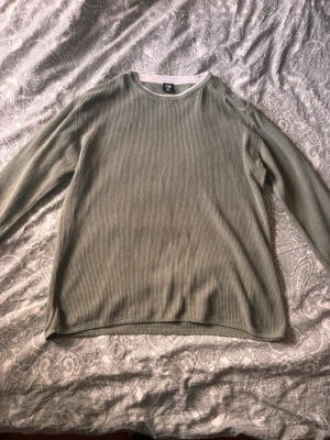 Olivgrön stickad tröja från FSBN - Säljer en olivgrön stickad tröja från FSBN i storlek L. Tröjan har rund halsringning med vit kant och är ribbstickad över hela plagget. Slim fit-modell med långa ärmar, perfekt för lager på lager och en clean look.