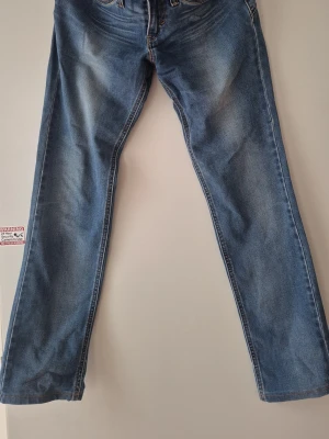 Levi's Demi Curve Low Rise Jeans - Snygga blå Levi's Demi Curve jeans med low rise och raka ben. Klassisk femficksmodell med slitningar och kontrastsömmar. Perfekta för dig som gillar en avslappnad men ändå stilren look. Tillverkade i mjuk och slitstark denim.