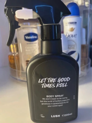 LUSH Let The Good Times Roll Body Spray - En svart sprayflaska med texten 'Let The Good Times Roll' från LUSH. Kroppssprayen har en söt och smörig popcorn-doft och rymmer 200 ml. Flaskan har en praktisk sprayfunktion och modern design, perfekt för dig som vill dofta gott hela dagen.