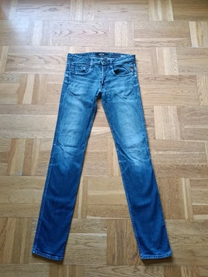 Blå jeans från Replay - Säljer ett par klassiska blå jeans från Replay med snygg tvätt och fem fickor. Jeansen har normal midja, raka ben och slitna detaljer för en avslappnad look. Tillverkade i bomull med en skön passform. Perfekta till din vardagsstil!
