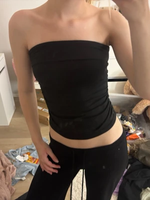 Svart bandeau tubtopp - Säljer en svart bandeau tubtopp med enkel och stilren design. Toppen är axelbandslös och har lätt rynkade sidor för en snygg passform. Perfekt att matcha med jeans eller kjol för en trendig look.