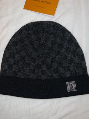 Louis Vuitton svart mössa med rutmönster - Snygg svart mössa från Louis Vuitton med klassiskt rutmönster och vikbar kant. skick 10/10 ingen konstig med den box finns ej 