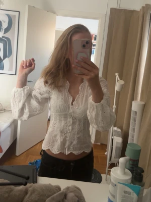 Vit broderad blus med puffärmar - Säljer en söt vit blus med broderade detaljer och v-ringning. Blusen har långa puffärmar och knappstängning framtill. Materialet är lätt och luftigt. Den har en feminin passform och fina spetskanter.