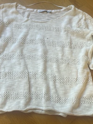Vit stickad tröja med strukturmönster - Säljer en vit stickad tröja med rund hals och korta ärmar. Tröjan har ett diskret strukturmönster i horisontella ränder som ger en snygg och enkel look. Perfekt att matcha med jeans eller kjol för en avslappnad stil.