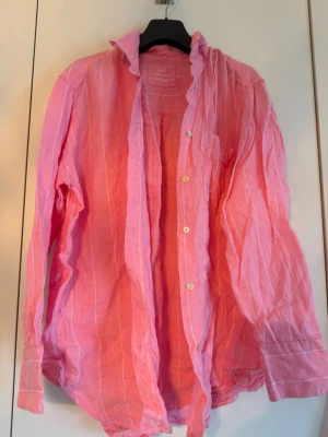 Rosa linneskjorta från M&S - Rosa långärmad skjorta i 100% linne. Skjortan har tunna vita ränder, klassisk krage och knäppning framtill. Perfekt för dig som gillar en avslappnad och luftig stil.