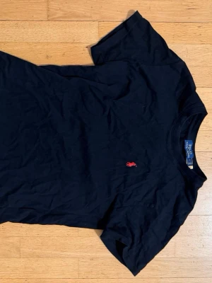 Svart t-shirt från Polo Ralph Lauren - Klassisk svart t-shirt från Polo Ralph Lauren med röd broderad logga på bröstet. T-shirten har rund halsringning och korta ärmar. Tillverkad i mjuk bomull som känns skön mot huden. Perfekt basplagg till garderoben.