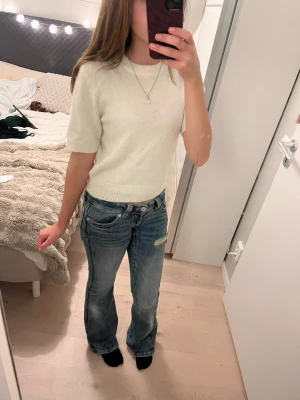 Vit stickad kortärmad tröja - Säljer en enkel och stilren vit stickad tröja med korta ärmar och rund hals. Tröjan har ribbade muddar vid ärmslut och nederkant, vilket ger en snygg passform. Perfekt att matcha med jeans eller kjol för en clean look.