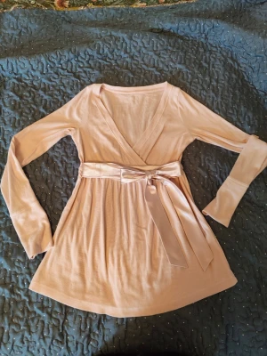Ljusrosa babydoll omlottopp med knytband från Hollister  - Supersöt ljusrosa babydoll omlottopp med långa ärmar och ett brett knytband i midjan. Toppen har v-ringad hals och är gjord i ett mjukt, stretchigt material som känns skönt mot huden. Det är inte riktigt en omlott topp utan det är bara överdelen av tröjan som går omlott, man kan liksom inte öppna den helt som en kofta. Supergullit med spettslinne under. Säljer den för att den är för stor på mig, då jag beställde fel storlek när jag köpte den🥲 Jag har användt den få gånger pga det.