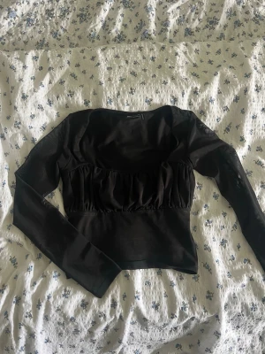 Topp från ASOS design  - Snygg svart långärmad topp från ASOS DESIGN med rynkad detalj under bysten, fyrkantig urringning och mesh armar. Perfekt festplagg eller bara som en finare topp som passar till allt. Knappt använd och ser ut som nu. Storlek 34