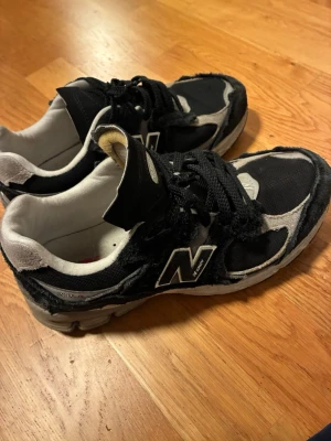 Svarta New Balance 2002R sneakers - Svarta och grå New Balance 2002R sneakers med klassisk N-logga på sidan. Skorna har mesh- och mockadetaljer, vita innersulor och grå sula. Snygg chunky siluett och snörning framtill. Perfekta för dig som gillar streetwear och sportig stil.