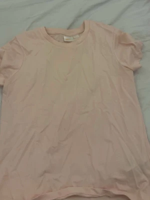 Ljusrosa t-shirt från Gina Tricot - Enkel och stilren ljusrosa t-shirt från Gina Tricot. Klassisk rund halsringning och korta ärmar. Perfekt basplagg i mjuk bomull som passar till allt. Snygg att styla med jeans eller kjol för en avslappnad look.