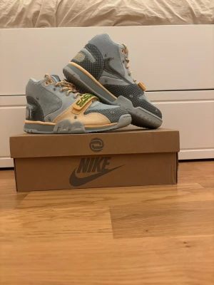 Travis scott air trainer 1 - Unika Nike sneakers i samarbete med Cactus Corporation. Skorna har en mix av ljusgrått, beige och grönt med detaljer i mesh och mocka. Tjocka snören och kardborreband med 'CACT.US CORPORATION' i grönt ger en cool vibe. Perfekta för dig som vill sticka ut.