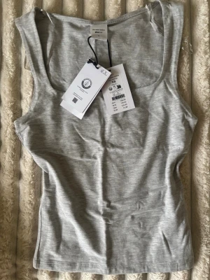 Ljusgrå linnetopp från gina tricot - Säljer en enkel och stilren ljusgrå linnetopp från gina tricot. Toppen är ärmlös med breda axelband och har en mjuk, stretchig känsla. Perfekt att matcha med jeans eller kjol för en clean look.