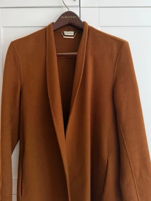 Kamelbrun kappa från By Malene Birger - Stilren kamelbrun kappa från By Malene Birger i mjukt ullmaterial. 