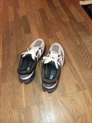 OnCloudsurfer Sneakers  - Säljer ett par snygga sneakers från On i grått, svart och vitt Helt oanvänt med vita skosnören och svarta detaljer blå. Skorna har en sportig design och meshpartier för bra ventilation.  Perfekta för dig som gillar stilrena och bekväma sneaker butikspris 2499 kronor 