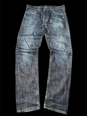 Blå archive grisch y2k 2000s washed jeans från levis - Klassiska blå jeans från Levi's med rak passform och fem fickor. Jeansen har slitningar och en tvättad look som ger en avslappnad vibe. Tillverkade i denim med kontrastsömmar och ikonisk läderpatch bak i midjan.