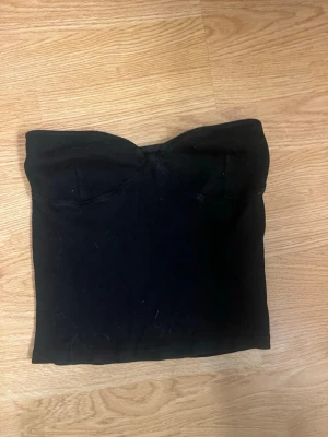 Svart tubtopp från Gina Tricot - Säljer en svart tubtopp från Gina Tricot med kupor och korsning fram, har även silikon så den inte glider! Storlek S men passar även XS