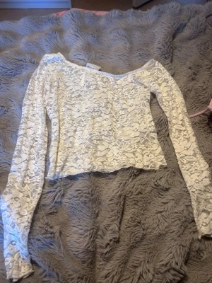 Vit långärmad spetsblus - Säljer en vit långärmad topp i genomskinlig spets med blommigt mönster. Toppen har en rak passform och bred urringning, perfekt för dig som gillar romantisk och trendig stil. Materialet är tunt och stretchigt för en bekväm känsla.