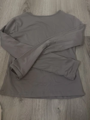 Grå långärmad basic tröja - En enkel och stilren grå långärmad tröja i mjukt material. Perfekt att ha som basplagg och funkar till det mesta. Tröjan har rund halsringning och en rak passform.