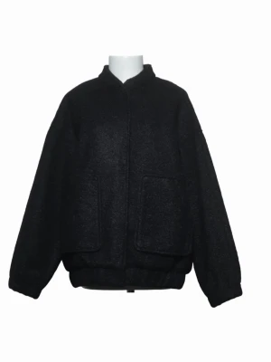 Svart oversized bomberjacka - Stilren svart bomberjacka i oversized modell med två stora framfickor och ribbade muddar vid ärmslut och midja. Jackan har en hög krage och är tillverkad i ett mjukt, ull-liknande material som ger en trendig och avslappnad look.
