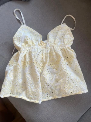 Vit broderad linnetopp från Subdued - Söt vit och gul linnetopp från Subdued med tunna axelband och broderade spetsdetaljer. Toppen har elastisk midja och v-ringad halsringning. Perfekt för varma dagar. Använd ca 3 gånger och köpt i London💕💕