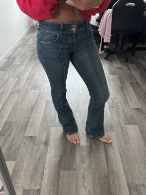 Mörkblå bootcut jeans med dubbla knappar - Säljer ett par mörkblå bootcut jeans med dubbla knappar i midjan och markerade sömmar framtill. Jeansen har klassisk femficksdesign och är tillverkade i stretchigt denimtyg som sitter snyggt på kroppen. Perfekta för en trendig och avslappnad look.