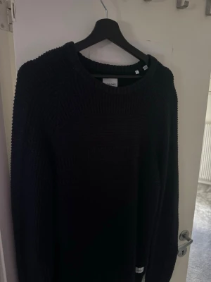 Mörkblå stickad tröja Jack & Jones - Snygg mörkblå stickad tröja från Jack & Jones med rund halsringning och grovstickat mönster. Perfekt för kyliga dagar och enkel att matcha med jeans eller chinos. Klassisk modell med ribbade muddar vid hals, ärmslut och nederkant.