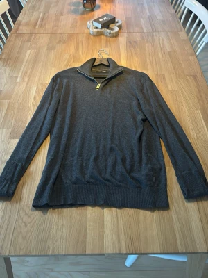 Mörkgrå tröja med halv dragkedja från Jack & Jones - Mörkgrå långärmad tröja med halv dragkedja i halsen och ribbade muddar vid ärmslut och nederkant. Perfekt för lager-på-lager och enkel att matcha med olika outfits.