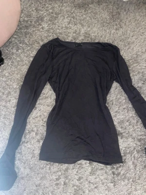 Svart långärmad topp - En enkel och stilren svart långärmad topp med rund hals. Toppen har en tight passform och är perfekt att matcha med olika outfits. Tillverkad i ett mjukt och stretchigt material som känns skönt mot huden.