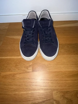 Mörkblå sneakers från Björn Borg - Snygga mörkblå sneakers från Björn Borg i mocka med vita sulor och svarta skosnören. Klassisk låg modell med enkel design och diskret logga på plösen. Perfekta för en stilren och avslappnad look. Pris kan diskuteras vid snabb affär.