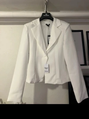 Vit kavaj från Boohoo - Stilren vit kavaj från Boohoo med klassisk krage och enkelknäppning framtill. Kavajen har en rak passform och är tillverkad i ett slätt tyg som ger en fräsch och modern look. Perfekt för att lyfta vilken outfit som helst. Helt ny med prislapp 