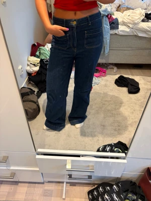 Mörkblå raka jeans med hög midja - Säljer ett par mörkblå jeans med raka ben och hög midja. Jeansen har två stora framfickor och tydliga sömmar i kontrastfärg. Klassisk femficksmodell med knapp och dragkedja framtill. Perfekta till en avslappnad stil.