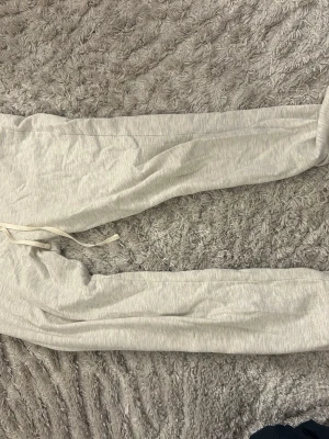Ljusgrå mjukisbyxor med dragsko - Säljer ett par ljusgrå mjukisbyxor med dragsko i midjan och smal passform. Byxorna har resår i bensluten och är tillverkade i ett mjukt, stretchigt material som är perfekt för chill dagar. Perfekta för dig som gillar en enkel och clean stil.