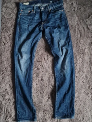 Levis jeans - Säljer ett par klassiska blå jeans med raka ben och snygga slitningar. Jeansen har fem fickor, knappgylf och kontrastsömmar. Materialet är denim i bomull. Nästan helt nya. Använda 5gngr. 