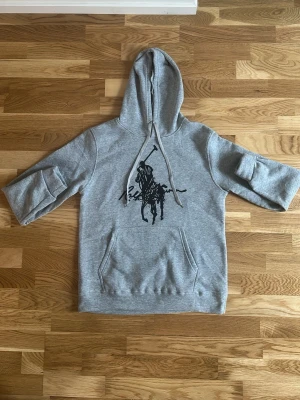 Grå hoodie med svart tryck - Snygg grå hoodie med stor svart häst- och ryttare-tryck på bröstet. Hoodien har huva med dragsko, känguruficka framtill . Perfekt för en avslappnad streetstil.