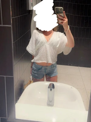 Vit blus med v-ringning - Säljer en luftig vit croppad blus med v-ringning och vida ärmar. Toppen har fina spetsdetaljer längs kanterna. 