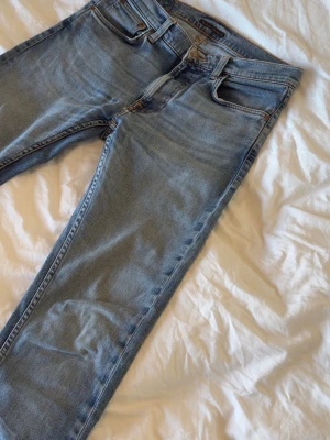 Ljusblå nudie jeans - Mått:  Midja 42cm Lår 24cm Knä 18cm Benöppning 17cm Längd 107cm Några undringar är det bara att fråga.