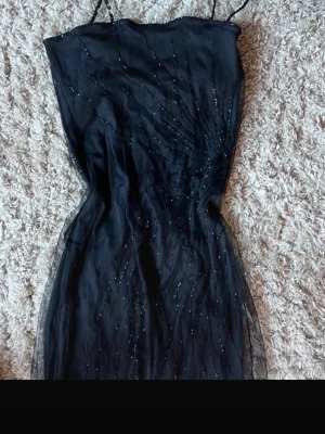 Svart glittrig klänning - Säljer en svart kort klänning med tunna axelband och glittriga detaljer. Klänningen har en figurnära passform och är tillverkad i ett tunt, lätt material som ger en elegant look. 