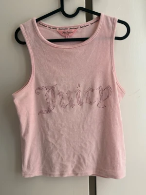 Rosa linnetopp från Juicy Couture - Säljer en ljusrosa linnetopp från Juicy Couture med glittrande stenar som stavar 'Juicy' på framsidan. Toppen är i sammet, ärmlös och har en klassisk rund halsringning.