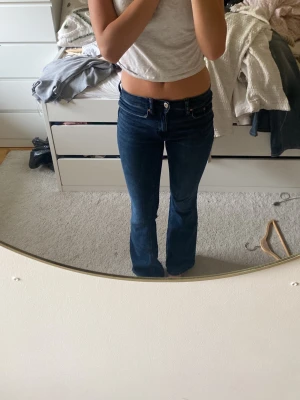 Mörkblå bootcut jeans - Säljer ett par mörkblå bootcut jeans med klassisk femficksdesign och normalhög midja. Jeansen har en lätt utsvängd passform nedtill och är tillverkade i denim med lite stretch för extra komfort. Perfekta för en avslappnad och trendig look.