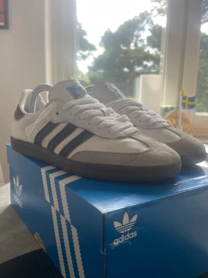 Adidas Samba vita och svarta sneakers - Klassiska Adidas Samba sneakers i vitt och svart med de ikoniska tre ränderna på sidan. Skorna är använda men de finns fortfarande mycket liv kvar i de! Står öppen för byten och pris kan diskuteras! 