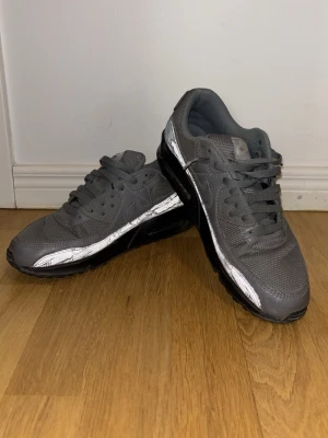 Grå Nike Air Max sneakers - Snygga grå Nike Air Max sneakers med svart sula och reflexmaterial som speciell detalj. Skorna har använts en del och därför kan jag gå med på att sänka priset, om köparen agerar snabbt. Nypriset ligger på ca 1899 kronor. Skolåda förekommer ej och storleken är 42,5.